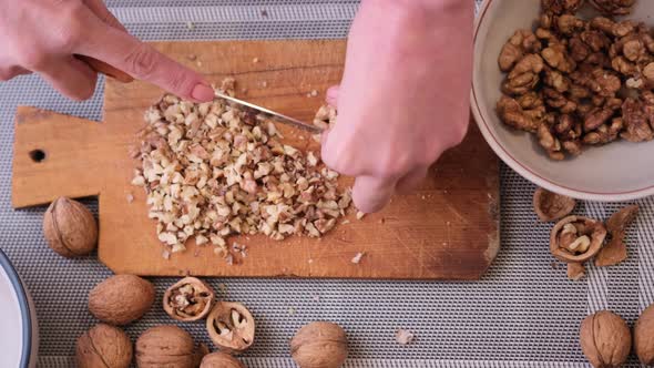 Chopping Walnuts Cores with Kitchen Knife on a Wood Cutting Board