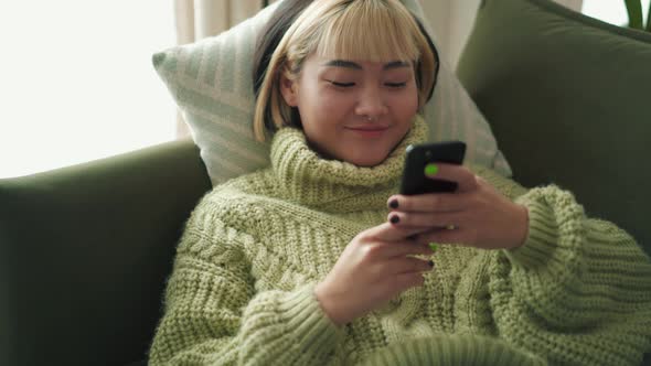 Smiling Asian woman typing by phone