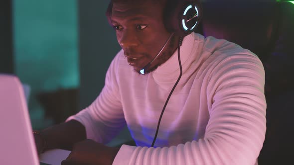 Black Man with Illuminated Headphones, Following the Game on His Laptop