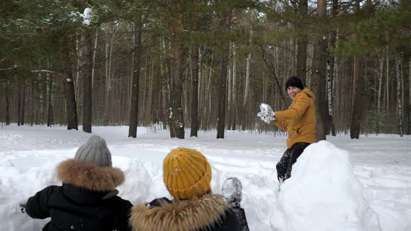 Man is Playing Snowballs with His Family Wife and Little Son Hiding Before Snow Wall