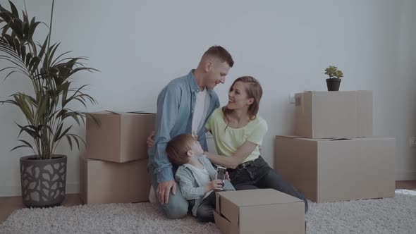 Image of Happy Couple with Children Sitting on Floor Among Cardboard Boxes