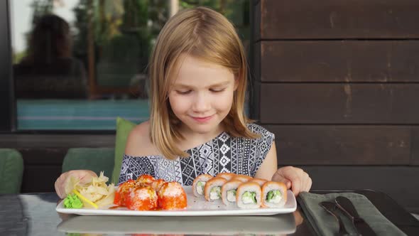 Little Girl in Cafe Restaurant Country House Smiles and Licks Looks Sushi Rolls