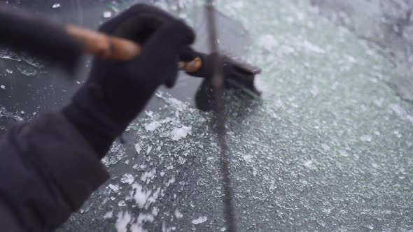 Man cleaning and scraping ice from car windshield in snow slowmo