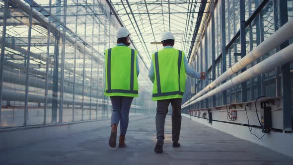 Engineers Discussing Problem Walking in Glasshouse Analysing Production Process