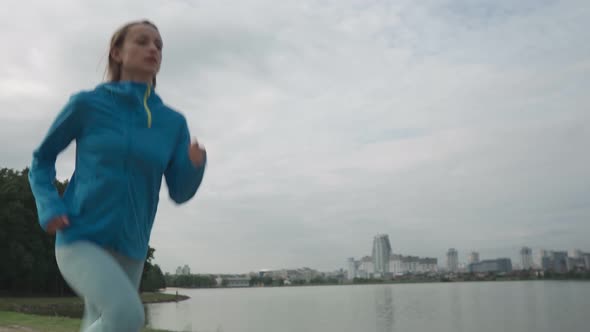 Young Sportswoman in Sportswear Trains in a Park Near the River