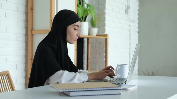 A Beautiful Muslim Female Student is Typing on a Laptop Keyboard