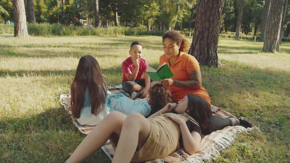 Teacher Asking Questions From Book to Multiracial School Kids Outdoors