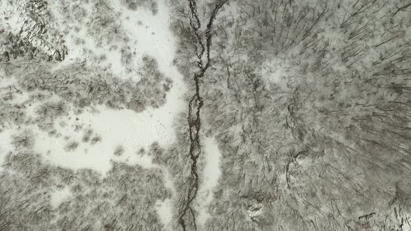 River stream flows in snow covered winter forest, aerial overhead