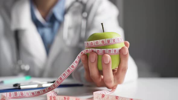 Nutritionist Doctor Holds A Green Apple In His Hand, Measuring Tape Wrapped Around An Apple