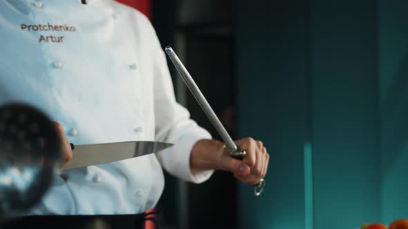 Restaurant kitchen: male chef sharpening knives before cooking steak