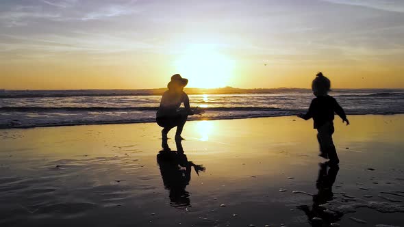 A child runs to mom's arms in 4k during a stunning sunset at the beach with a colorful sky.