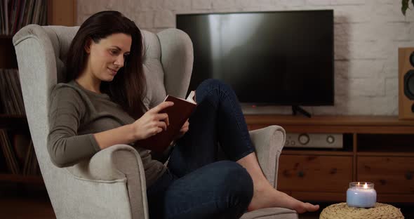 Young Woman Sits on an Armchair and Reads a Book