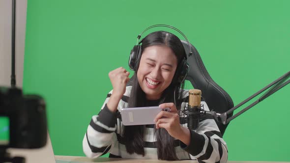 Woman With Headphone Celebrating Winning Mobile Phone Game While Shooting Video On Green Screen