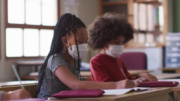 Group of kids wearing face masks writing while sitting on their desk at school