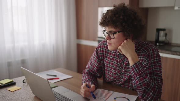 Brooding Serious Curly Freelancer Man Sit at Table in Comfortable Home Office Room Work on Laptop