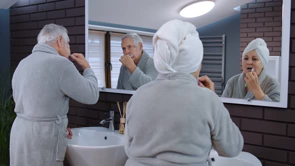 Senior Couple Man and Woman Brushing Teeth and Looking Into a Mirror at Luxury Bathroom at Home