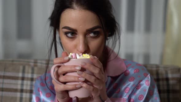 Portrait of Attractive Young Woman Drinking Hot Chocolate with Marshmallows and Watchinig Film in