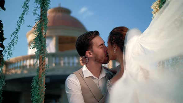 Beautiful newlyweds kiss while sitting on a swing in a Greek antique location