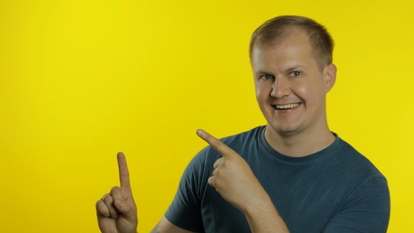 Portrait of Young Man Posing in Green T-shirt. Happy Smiling Guy Pointing at Something with Hand