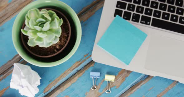 Laptop, sticky notes, pot plant, pencil, crumpled paper and binder clips