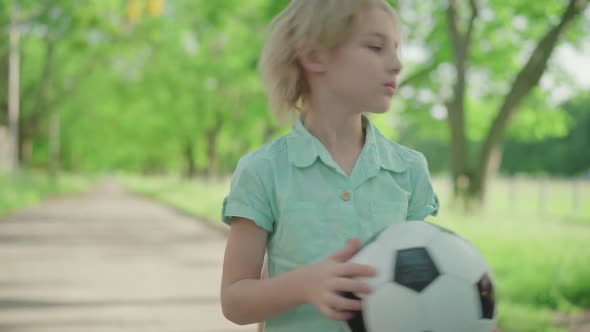 Middle Shot of Cute Blond Boy with Soccer Ball Yelling at Joyful Sister Running Around. Dissatisfied