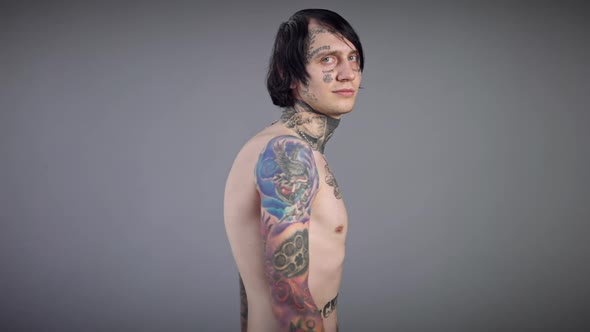 Man with Tattooed Torso Hands Neck and Face Turning Posing at Grey Background