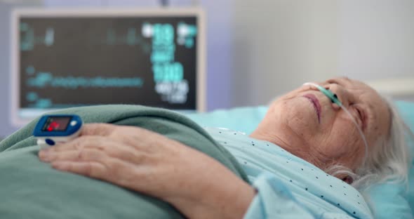 Elderly Female Patient with Oximeter on Finger Lying in Hospital Bed