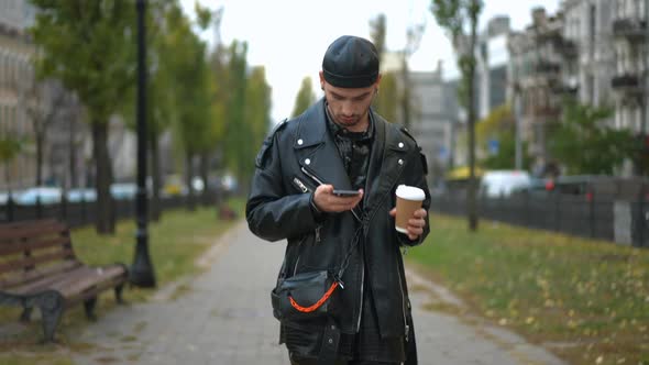 Portrait of Focused Gay Man Messaging Online on Smartphone Walking with Coffee Cup in the Morning