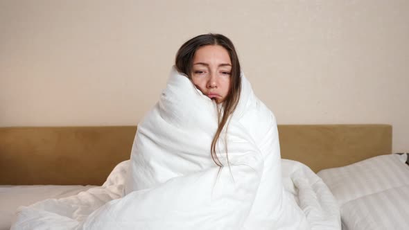 Sick Woman Wrapped with Soft White Duvet Sits in Bedroom