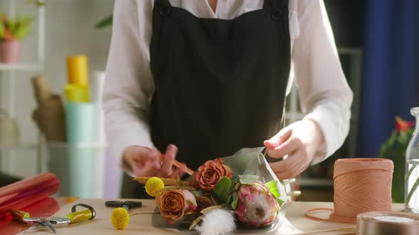 Young Florist Wrapping Bouquet of Roses and Dried Flowers Into Packaging Paper and Tying with Ribbon