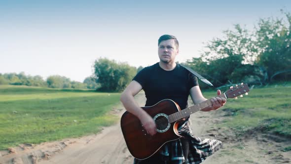 A Male Guitarist Is Walking Along the Road and Playing an Acoustic Guitar