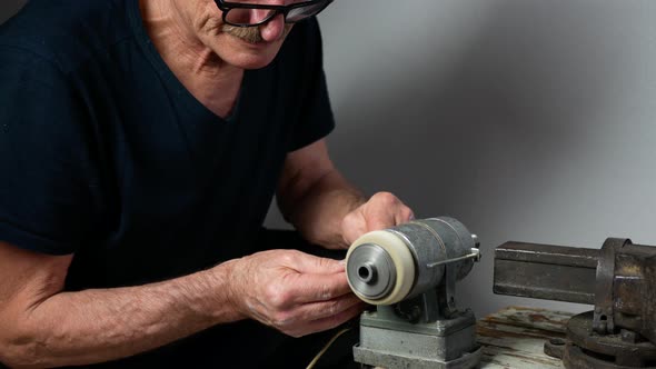 Old man with glasses is sharpening a tool using grinding machine