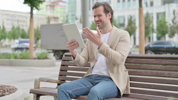 Upset Young Man Reacting to Loss on Tablet While Sitting on Bench