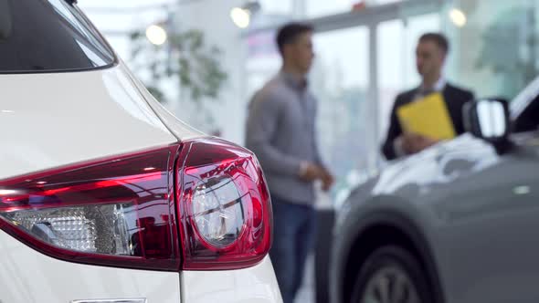 Car Lights on the Foreground, Man Buying Car at the Dealership on the Background