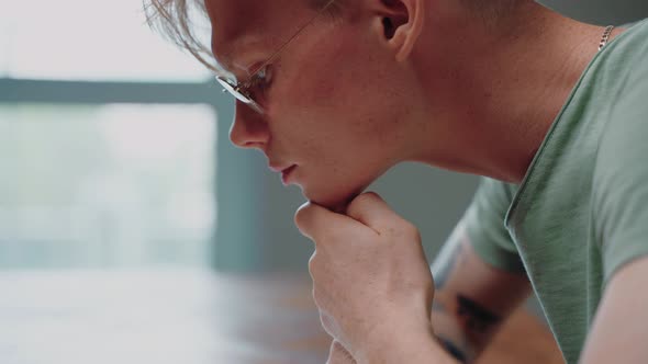 Young Man in Glasses Reading a Textbook and Stressing with His Fist in His Chin