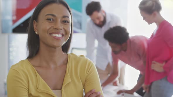 Portrait of happy biracial businesswoman over diverse colleagues in office