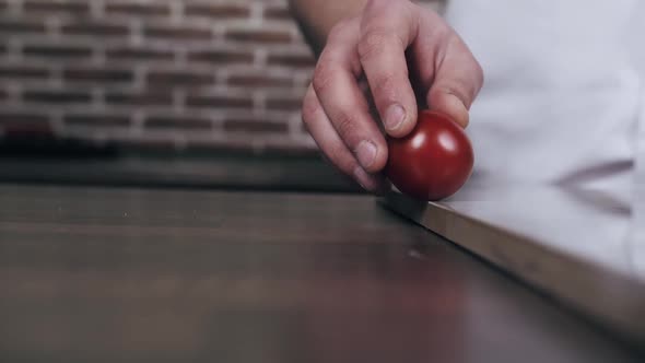 Chef is Rolling a Tomato Across the Cutting Board From One Hand to Another
