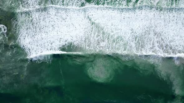 Aerial - Waves rolling out, white-wash with sandy bottom disturbed, ascending drone shot