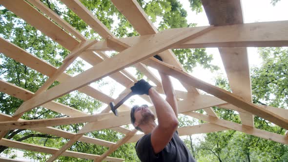 Man Makes Hammering Wooden Roof of House at the Start of Construction