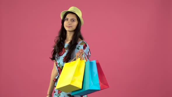 Girl Posing on Camera with Shopping Bags and Smiling. Pink Background. Slow Motion