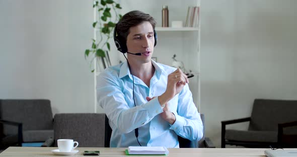 Young Focused Manager Call Agent Sits in Office, Wears Headphones with Head Microphone, Speaks