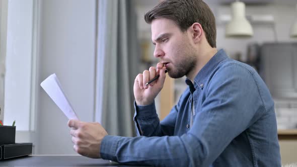 Focused Beard Young Man Reading Documents in Office