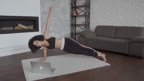 Young Multiracial Woman Doing Her Exercises at Home Using a Laptop To Repeat Moves From Video