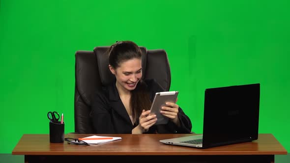 Worker Girl Sits at a Workplace Leaning Back in a Leather Chair and Communicates on a Tablet