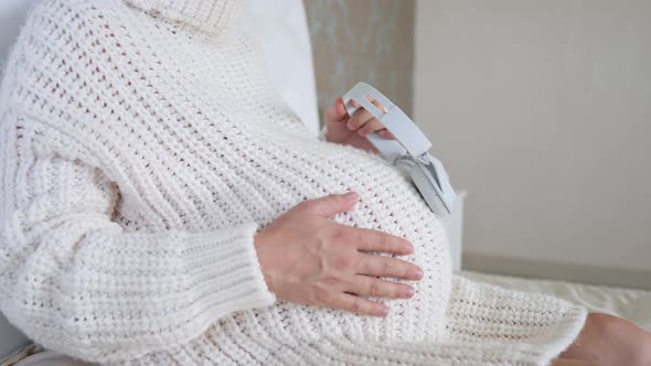 Pregnant Woman Resting On Bed With Headphones On Her Tummy