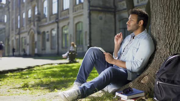 Multiracial Male Sitting on Grass Under Tree, Writing in Notebook, Creative Idea