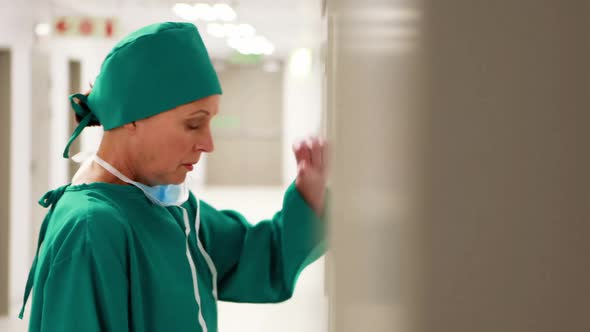 Tensed female surgeon leaning on wall in corridor