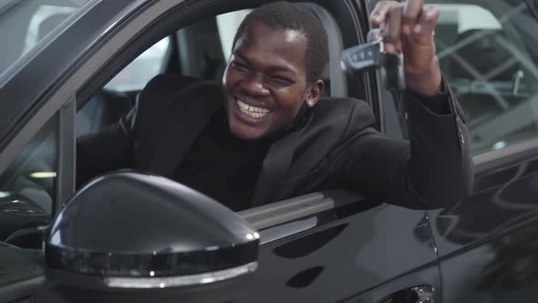 Close-up Face of Happy African American Man Sitting in Car Salon and Bragging Keys