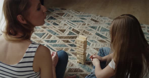 Mother and Daughter Build Tower From Wooden Bricks Sitting on a Floor at Home