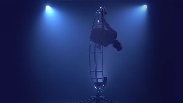 Gymnast in a Brilliant Costume Performs Tricks on a Special Design Moon . Blue Smoke Background